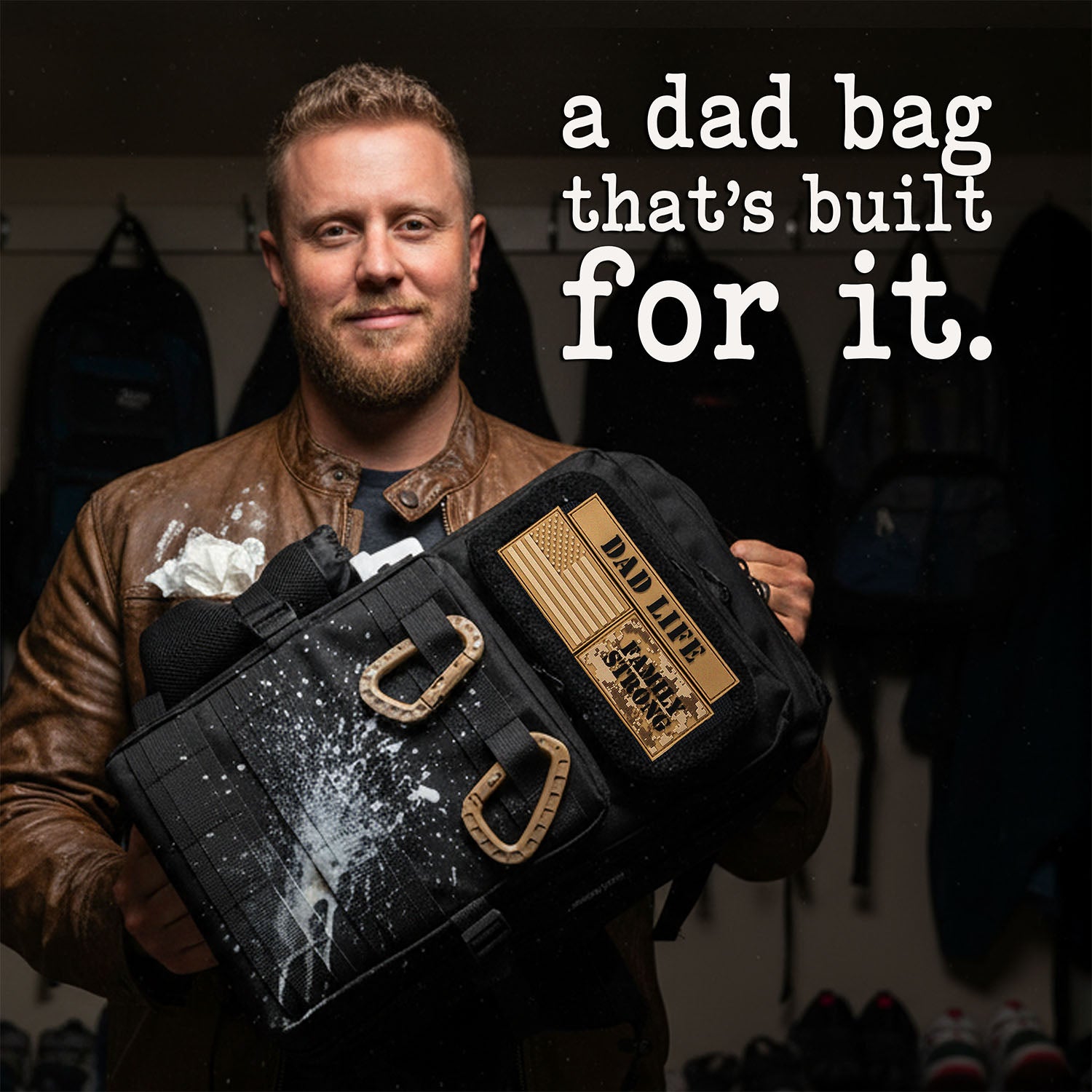 Man holding a black diaper bag for dads with 'Dad Life' patches, text 'a dad bag that's built for it.'