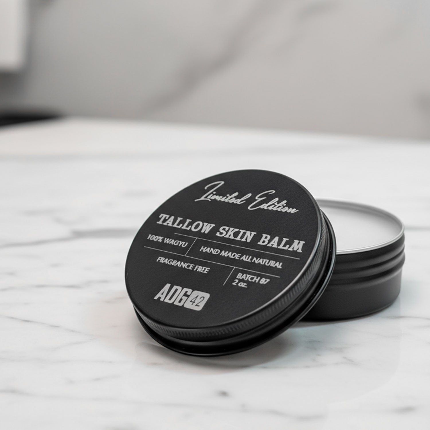 Black tallow skin balm container with lid on a marble surface