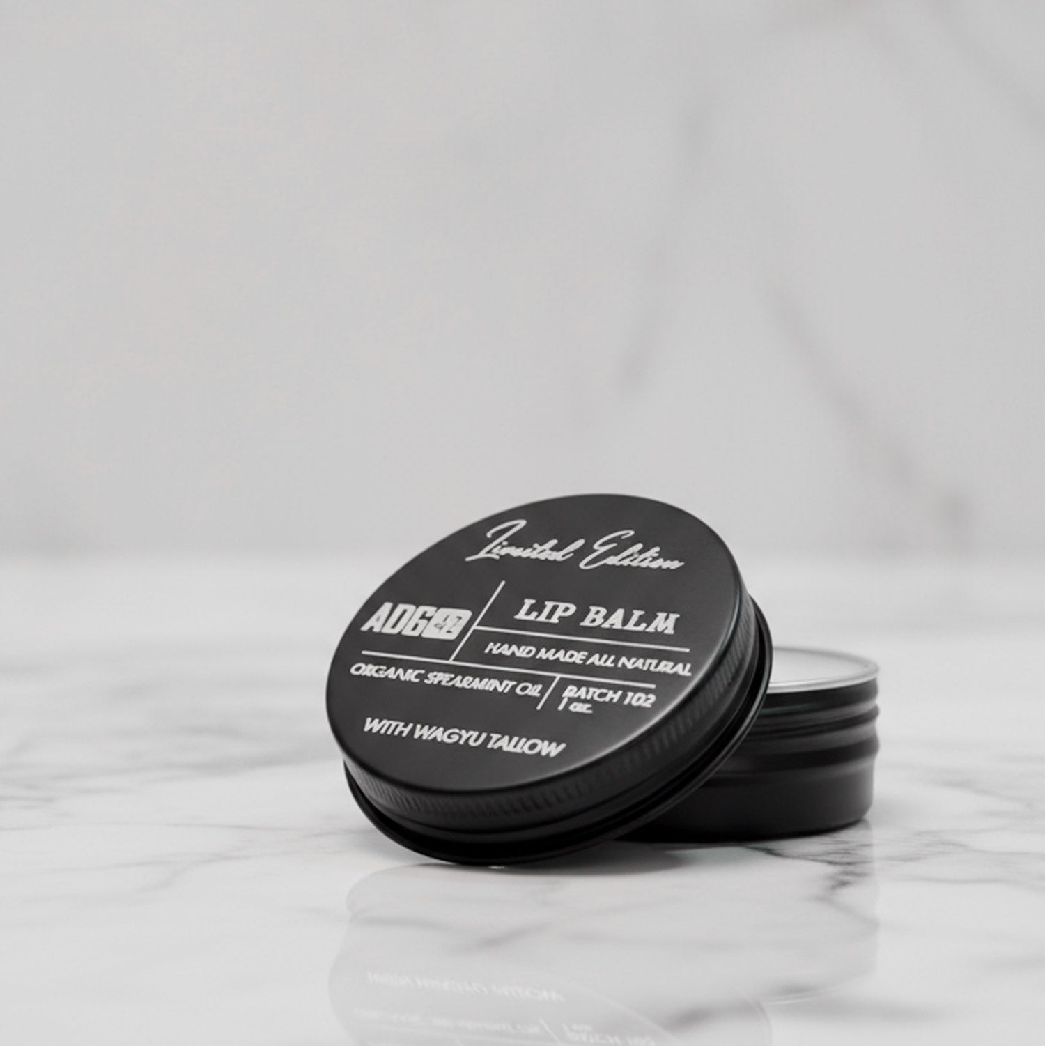 Lip balm container with black lid and white text on a light gray background