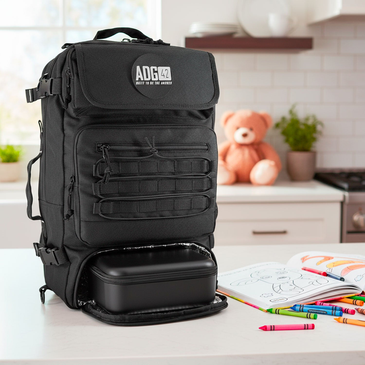 Black dad diaper bag backpack on a kitchen counter with coloring books and crayons