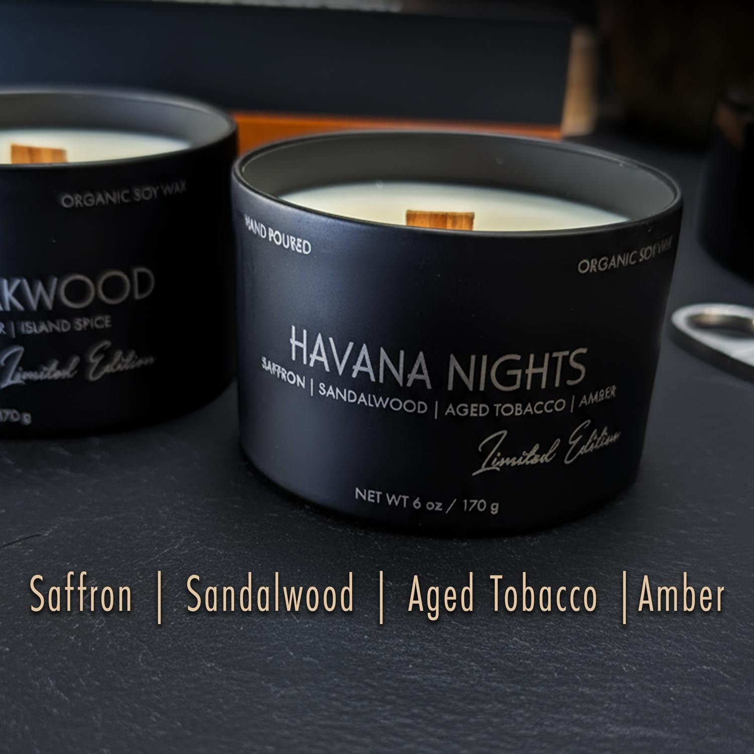 Two candles for men in black tins labeled 'Havana Nights' and 'Island Spice' on a dark surface.